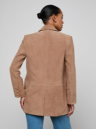 A woman with her hair in a bun wears the Aimee Oversized Suede Blazer in tan and blue jeans, facing away from the camera against a plain light background.