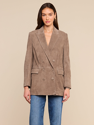 A woman stands against a beige background, wearing the Aimee Oversized Suede Blazer in taupe and blue jeans, her hands at her sides and her expression neutral.