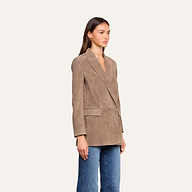 A woman stands facing left, wearing the Aimee Oversized Suede Blazer in taupe with a boyfriend fit, paired with blue jeans against a plain light background.