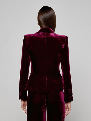A person with straight brown hair is seen from behind wearing the L'AGENCE Marie Velvet Blazer in maroon, with matching pants, standing against a plain light gray background.