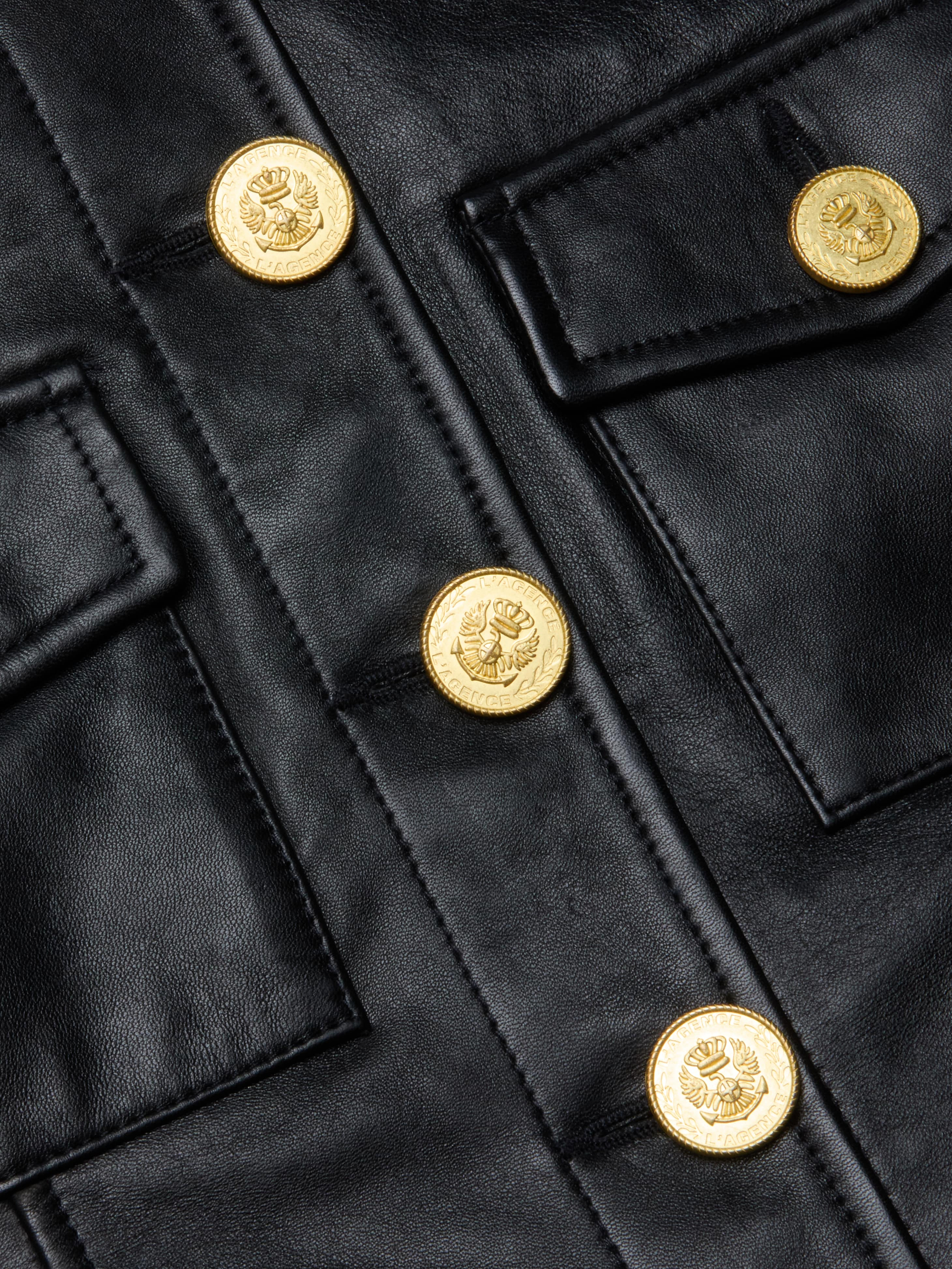 Close-up of the Kumi Cropped Leather Jacket in black leather, featuring gold embossed buttons and two flap pockets.