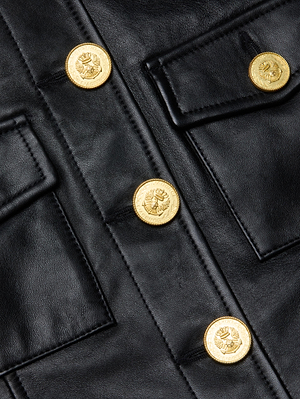 Close-up of the Kumi Cropped Leather Jacket in black lambskin, featuring two flap pockets and five shiny gold buttons adorned with a detailed lion head design.