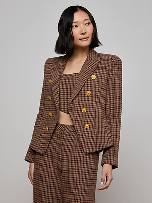 A woman with chin-length dark hair wears the L'AGENCE Bethany Houndstooth Blazer with heritage tailoring and lion head buttons, paired with a matching cropped top, as she stands against a light gray background.