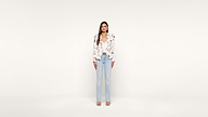 Woman stands facing forward, wearing a white floral blazer, white top, light blue jeans, and open-toed heels, against a plain white background.
