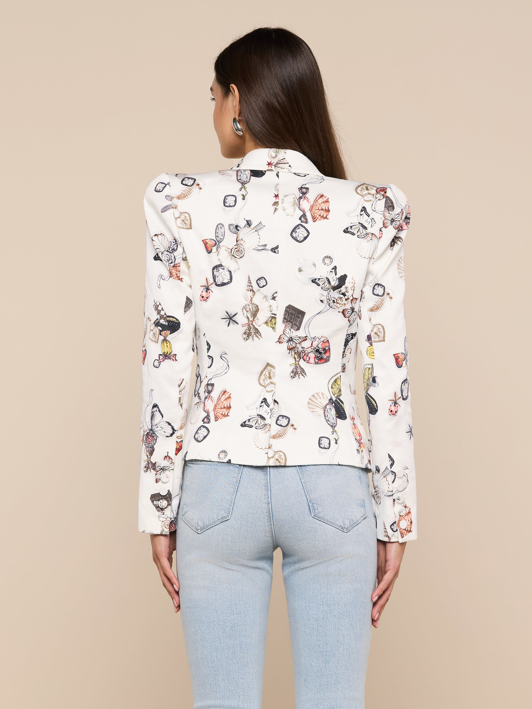 A woman with long brown hair is shown from the back against a plain background, wearing the Bethany Structured Blazer with a butterfly print and light blue jeans.