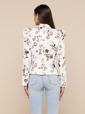 A woman with long brown hair faces away, wearing the Bethany Structured Blazer featuring colorful, whimsical illustrations and light blue jeans against a beige background.