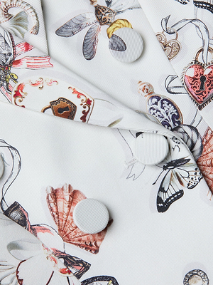 Close-up of the Bethany Structured Blazer in white, featuring whimsical prints of butterflies, teacups, and ornate keys, detailed with three round white buttons along the seam.