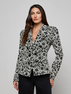 A woman with long brown hair models the Bethany Flocked Tweed Blazer with black buttons and black pants, posing against a plain light gray background.