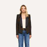A woman faces forward against a plain light background, wearing the Imogen Satin Lapel Blazer—a double-breasted black blazer with gold vertical stripes and a satin lapel—paired with a white top, blue jeans, and a black belt with a gold buckle.