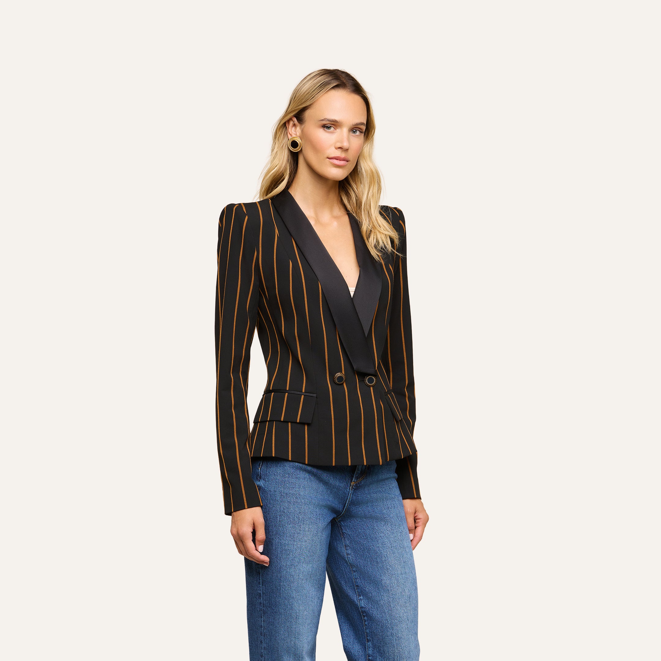 A person wearing the Imogen Satin Lapel Blazer—black with gold vertical stripes—paired with blue jeans stands against a plain, light background.