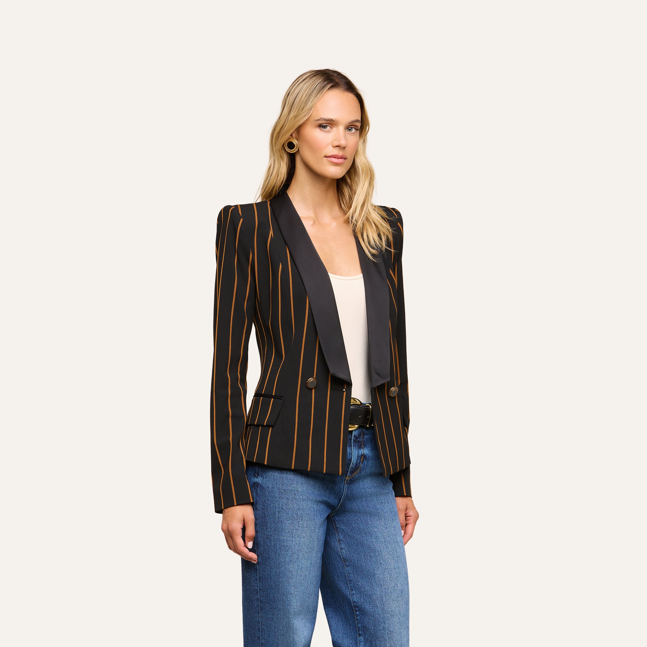 A woman stands facing forward, wearing the Imogen Satin Lapel Blazer—featuring yellow vertical stripes—over a white top and blue jeans, against a plain light background.