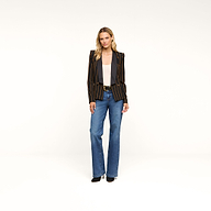 A woman stands facing forward against a plain white background, wearing the Imogen Satin Lapel Blazer—a black double-breasted blazer with a satin lapel—paired with a light gray top, blue jeans, and black shoes.