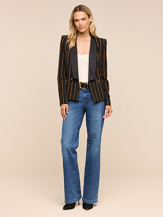 A woman stands facing forward, wearing the Imogen Satin Lapel Blazer with striking orange stripes and a satin lapel, paired with a white top, blue jeans, and black heels against a plain beige background.
