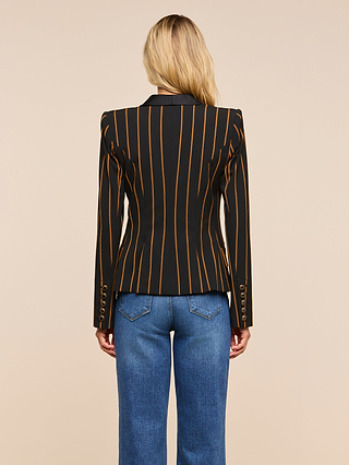 A woman with long blonde hair is facing away, wearing the Imogen Satin Lapel Blazer with vertical orange stripes and blue jeans, standing against a beige background.