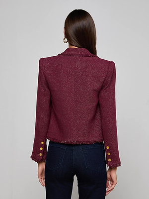 A woman with long brown hair is seen from the back wearing the Sylvia Tweed Jacket by L'AGENCE, featuring gold sleeve buttons, paired with dark blue jeans against a plain light gray background.