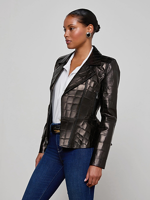 A woman models the L'AGENCE Lyric Leather Peplum Jacket, featuring black croc-embossed leather, styled over a white shirt and blue jeans. She stands sideways against a light background with her hair pulled back and hands at her sides.