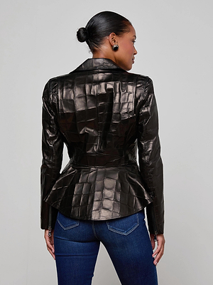 A woman with her hair in a bun models the L'AGENCE Lyric Leather Peplum Jacket, featuring shiny croc-embossed lambskin, paired with dark blue jeans. She faces away from the camera against a light gray background.