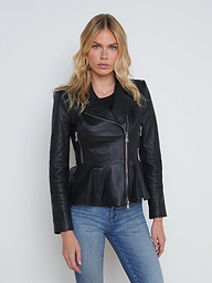 A woman with wavy blonde hair wears the Lyric Leather Peplum Jacket in black lambskin leather and blue jeans, standing against a plain off-white background, facing forward with a neutral expression.