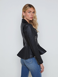 A woman with long blonde hair stands sideways against a plain light background, wearing the Lyric Leather Peplum Jacket in black lambskin over blue jeans.