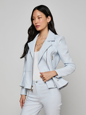 A woman with long dark hair wears the Lyric Peplum Biker Jacket in light blue over a white top and matching pants, standing against a plain gray background.