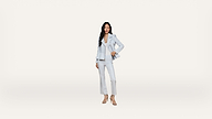 Woman in a light blue suit and heels stands confidently against a plain white background, one hand on her hip and the other relaxed by her side.