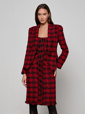 A woman with long brown hair poses against a plain background wearing the Kaisley Tweed Blazer by L'AGENCE in red and black, styled with a matching knee-length skirt. One hand rests by her side, the other gently touches her skirt.