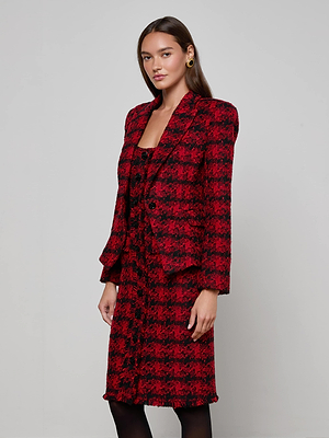 A woman stands against a plain background wearing the red and black L'AGENCE Kaisley Tweed Blazer with a matching knee-length skirt. She has long, straight brown hair and gold hoop earrings.