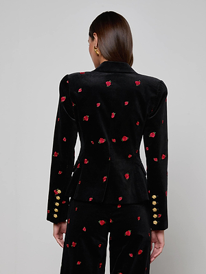 A woman faces away, wearing the L'AGENCE Kaisley Velvet Blazer in black with small red rose patterns and gold sleeve buttons. Her straight brown hair is tucked behind her ears against a plain light gray background.