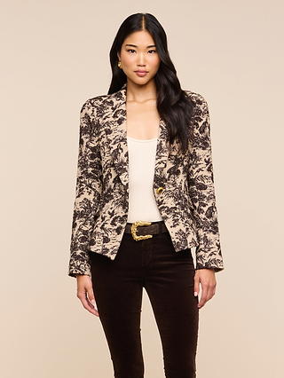 A woman with long black hair wears the Kaisley Blazer, featuring an antique-inspired print, paired with a beige top and dark pants. She stands facing forward against a light beige background, her expression neutral.