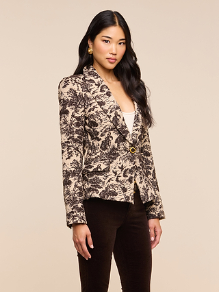 A woman with long black hair stands against a plain beige background wearing the Kaisley Blazer, which features an antique-inspired print, styled with a white top, dark pants, and gold earrings.