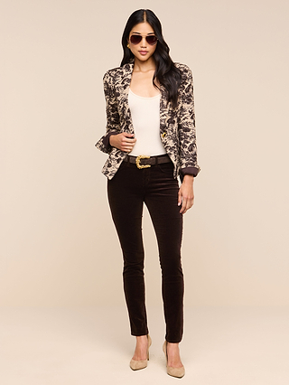A woman wearing sunglasses, the Kaisley Blazer with an antique-inspired print, a white top, black pants, and beige heels stands against a plain beige background.