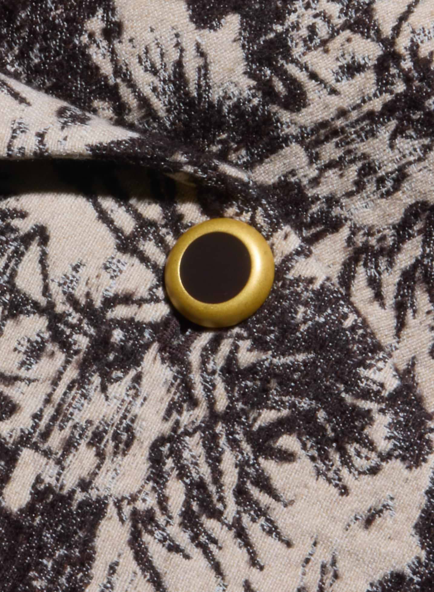 A close-up of a gold and black button on beige fabric adorned with the Kaisley Blazer’s dark, intricate leafy pattern, featuring its antique-inspired print.