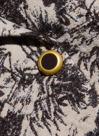 A close-up of a gold and black button on beige fabric with a black abstract or floral pattern, highlighting the elegant detailing characteristic of the Kaisley Blazer.
