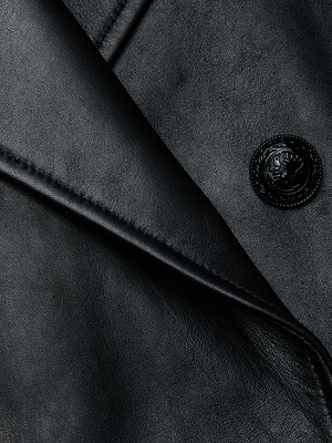 Close-up of the Xoey Cropped Leather Trench Coat in black Italian lambskin, highlighting a detailed seam, folded lapel, and a textured black button with an embossed design.