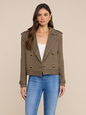 A woman wears the Xoey Cropped Trench Coat, a brown plaid double-breasted blazer with gold buttons, over a white top and blue jeans, standing against a plain beige background and looking at the camera.