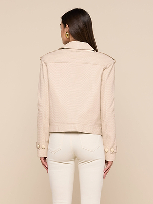 Une femme se tient debout, dos à lappareil photo, modélisant le trench-coat en cuir cropped de Xoey avec de gros boutons et le pantalon taille haute assorti, sur un fond beige uni.