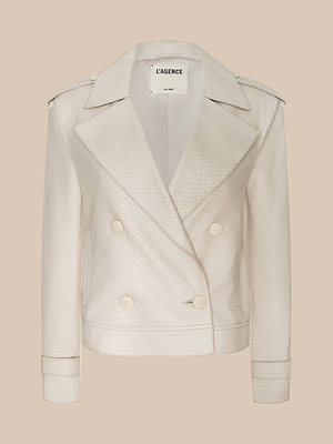 Le trench-coat en cuir raccourci Xoey de LAGENCE se compose dun cuir crème à double boutonnage avec une texture subtile de peau de serpent, de larges revers, dépaulettes et dune étiquette intérieure de la marque, affichée sur un fond beige.