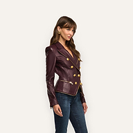A woman in an hourglass silhouette wears an Ottilie Leather Blazer in dark burgundy with gold buttons and zipper accents, paired with blue jeans for a look of power dressing.