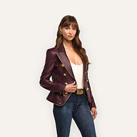 A woman in an hourglass silhouette wears an Ottilie Leather Blazer in burgundy with gold buttons over a white top and blue jeans, embracing power dressing.