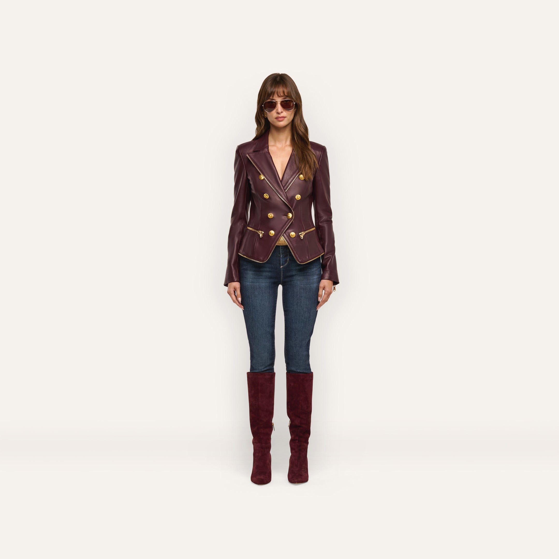 A person wearing an Ottilie Leather Blazer with gold buttons, dark wash jeans, and knee-high suede boots, showcasing a power-dressing hourglass silhouette.