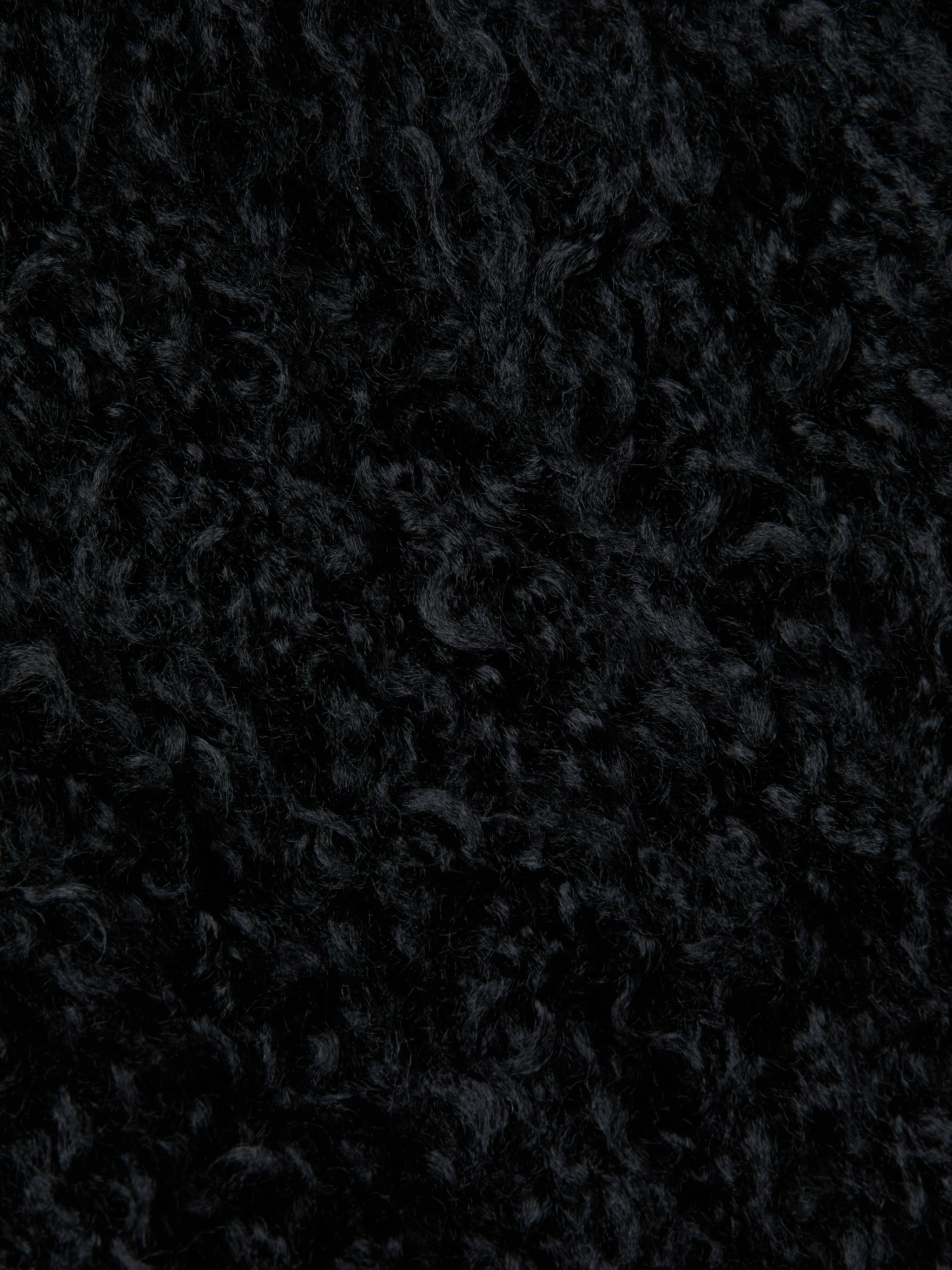 Close-up of the Aura Cropped Faux Fur Jacket in black, showcasing its dense and soft curly textured fabric that resembles shag faux fur.