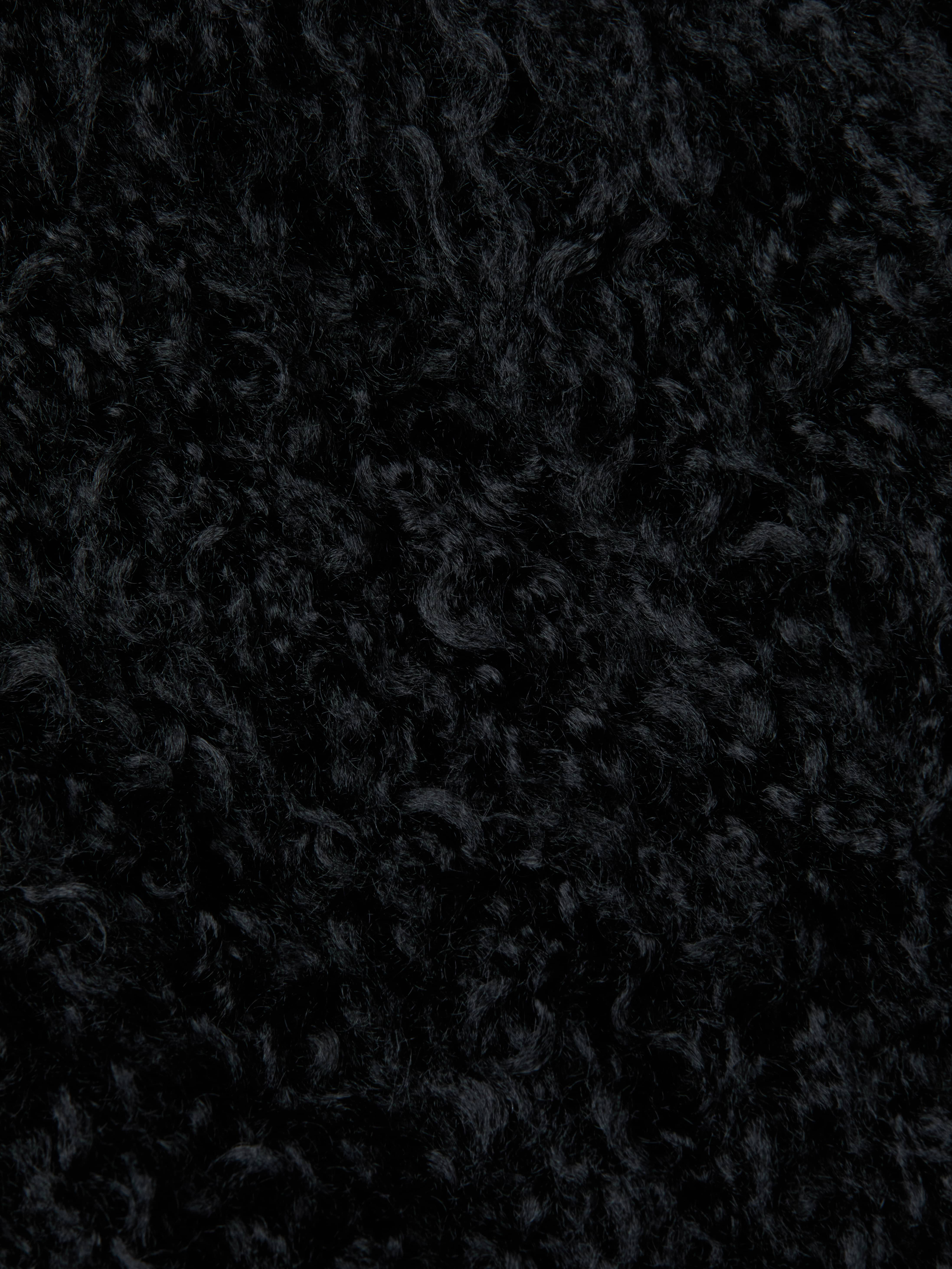 Close-up of the Aura Cropped Faux Fur Jacket in black, showcasing its dense and soft curly textured fabric that resembles shag faux fur.