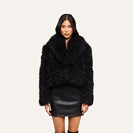 A woman wearing the Aura Cropped Faux Fur Jacket and a black leather skirt stands facing forward against a plain light background.