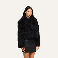 A woman with long dark hair wears the Aura Cropped Faux Fur Jacket and a black leather skirt, standing against a plain light background.