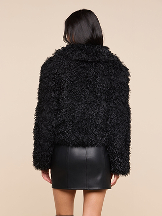 A person stands with their back to the camera, wearing the Aura Cropped Faux Fur Jacket paired with a black leather skirt against a plain beige background.