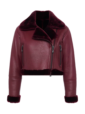 The Pike Shearling Leather Jacket is a cropped burgundy leather piece with plush lamb shearling collar and lining, asymmetrical front zip, zippered chest pockets, and rolled cuffs showing matching shearling—ideal for winter layering.