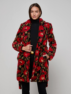 A woman wears the L’AGENCE Tristan Sherpa Midi Coat with a red poppy print over a black turtleneck and pants, standing against a light gray background with her hands in the coat’s pockets.