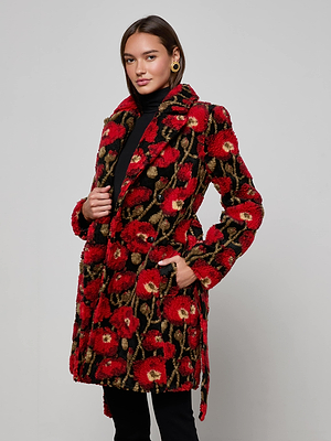A woman poses against a plain background wearing the L'AGENCE Tristan Sherpa Midi Coat in a red poppy print over a black turtleneck and pants, with one hand in her pocket and the other holding her Italian wool-blend coat.