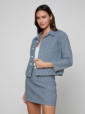 A woman wears the Nelly Cropped Jacket in blue and white vertical stripes with a matching mini skirt, standing against a plain light gray background and looking relaxed at the camera.