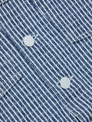 Close-up of the Nelly Cropped Jacket, showcasing its blue and white patterned textured cotton with diagonal lines, two white buttons, a pocket seam, and visible stitching detail.